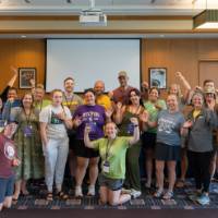 Full group photo of 40 participants cheering at workshop indoors